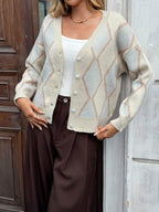 Woman showing off a cream argyle knit cardigan with a white tank top and brown pants.