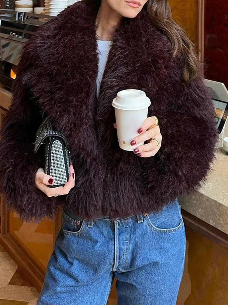 Close-up of a woman in a burgundy faux fur jacket holding a coffee cup and a sparkling clutch.