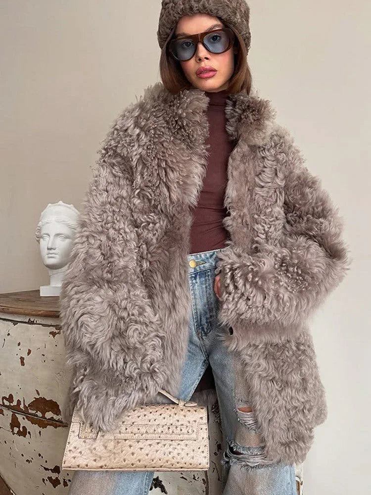 Close-up of a woman's upper body wearing a grey curly faux fur coat, highlighting the collar and texture.