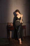 Woman wearing a black satin slip dress with lace bust detail and a matching black robe, leaning on a wooden table.