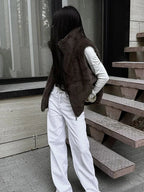 Woman wearing a brown faux fur vest over a white long-sleeved shirt and white wide-leg jeans, standing outdoors.