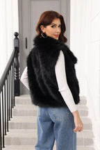 Woman wearing a black faux fur vest over a white top and blue jeans, turning to look over her shoulder.
