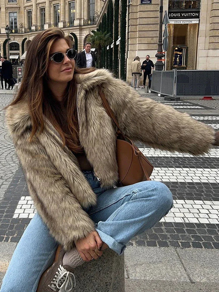 Woman wearing a brown faux fur jacket with a collared neckline and zipper closure, paired with light wash denim jeans and sneakers.