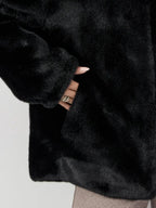 Close-up of a hand reaching into the pocket of a black faux fur jacket.