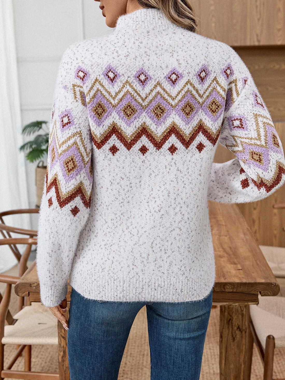 Woman wearing a white knit sweater with a geometric pattern in purple, brown, and gold.