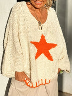 Close-up of a woman smiling, wearing an off-white knit sweater with an orange star graphic and orange trim.