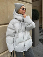Side view of a woman in a light gray puffer jacket, adjusting her hood.