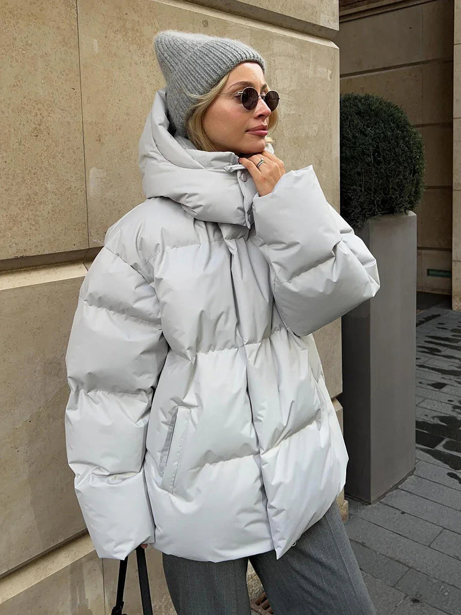 Side view of a woman in a light gray puffer jacket, adjusting her hood.