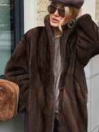 Close-up of a woman's face wearing large circular earrings, sunglasses, and a taupe beret, with the collar of a brown faux fur coat visible.
