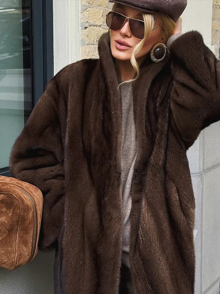 Close-up of a woman's face wearing large circular earrings, sunglasses, and a taupe beret, with the collar of a brown faux fur coat visible.