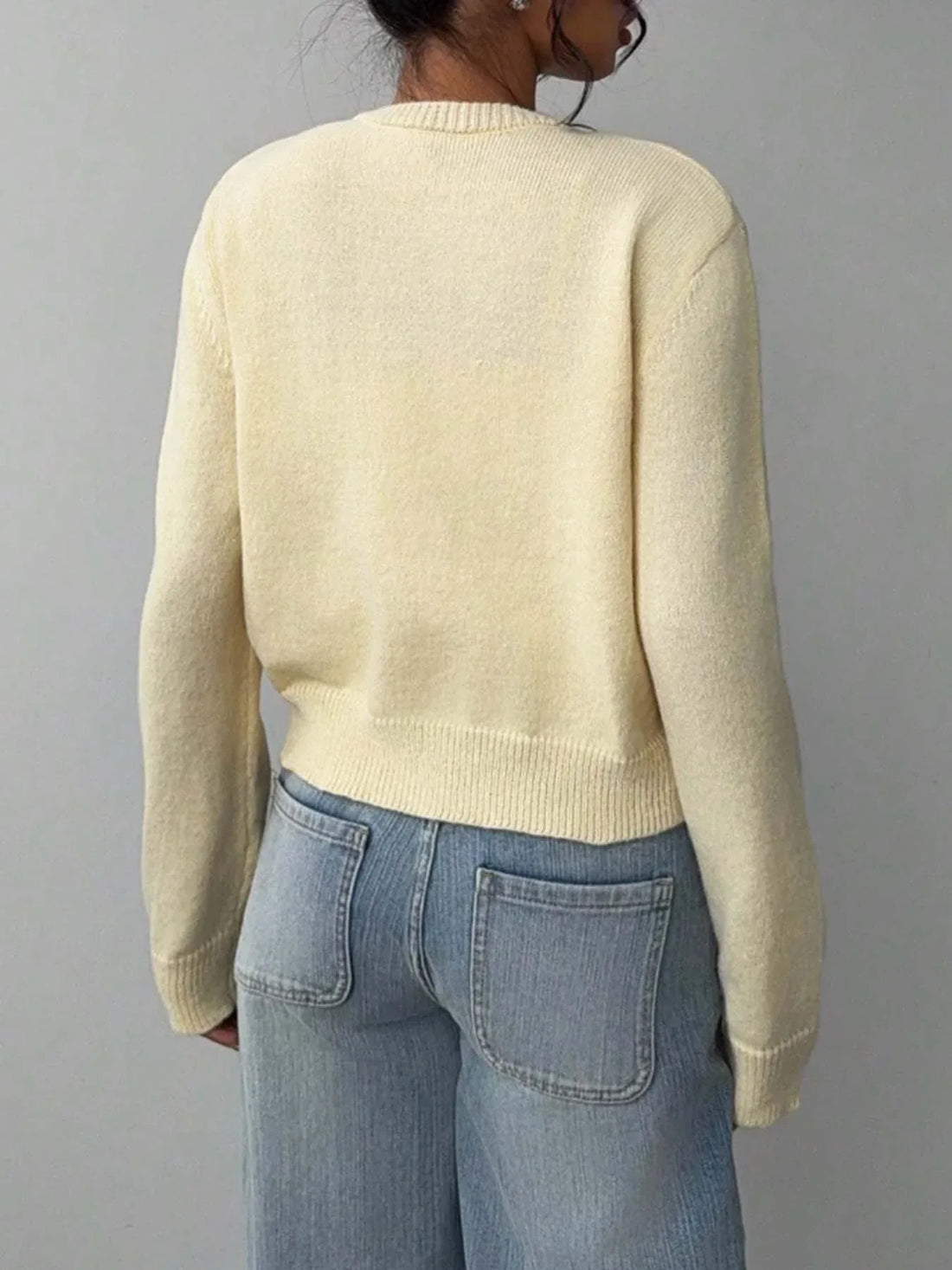 Woman wearing a light yellow button-front knit cardigan with long sleeves.