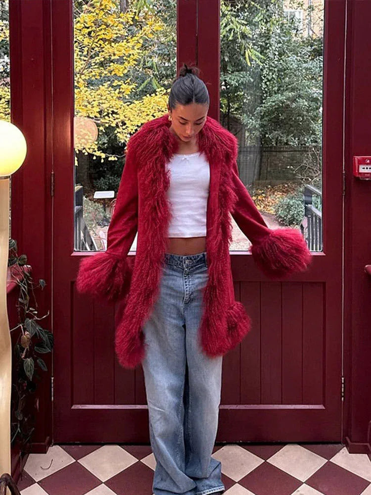 Woman wearing a red suede coat with faux fur trim and cuffs, paired with a white crop top and blue jeans.