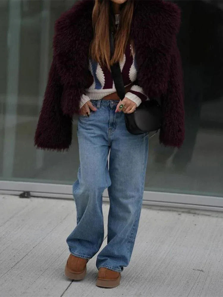 Full body shot of a woman in a burgundy faux fur jacket, striped sweater, and wide-leg blue jeans.