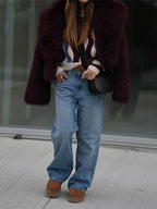 Full body shot of a woman in a burgundy faux fur jacket, striped sweater, and wide-leg blue jeans.