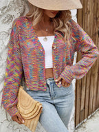 Woman wearing a rainbow multicolor open-knit cropped cardigan with a v-neck and button-front closure, accessorized with a straw hat and clutch, with a white top and blue jeans.