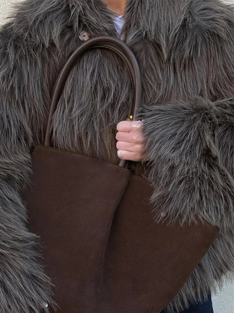 Close-up of a woman's hands holding a large brown tote bag, with the textured brown faux fur of her jacket visible.