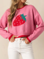 Woman wearing a pink cropped knit sweater with a red and green strawberry graphic on the front and red trim.