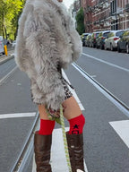 Back view of a woman wearing a light grey faux fur jacket and brown boots on a city street