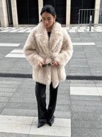 Full body shot of a woman in a cream faux fur coat with a belted waist.