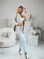 Full body shot of a woman in a beige oversized knit cardigan paired with light wash jeans and sneakers.