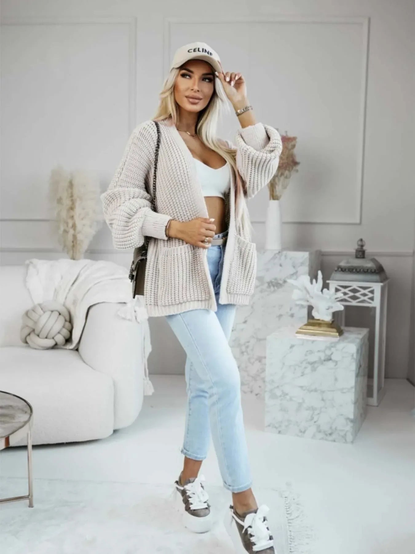 Full body shot of a woman in a beige oversized knit cardigan paired with light wash jeans and sneakers.