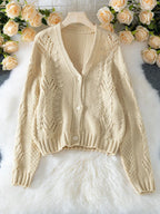 Beige cropped knit cardigan laid flat with V-neck and button closure, surrounded by artificial roses.