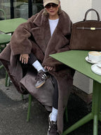 Woman sitting at an outdoor cafe table wearing a brown faux fur coat.