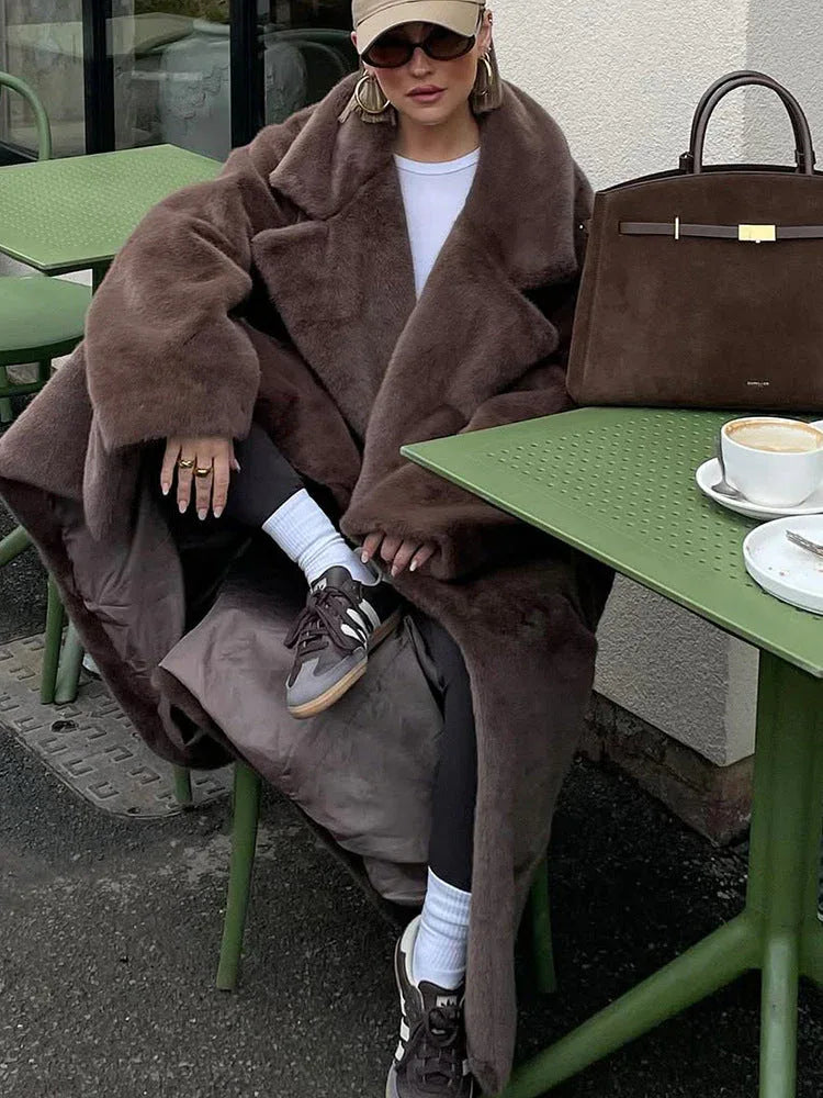Woman sitting at an outdoor cafe table wearing a brown faux fur coat.