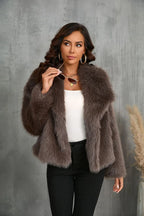Woman holding sunglasses while wearing a brown faux fur cropped jacket