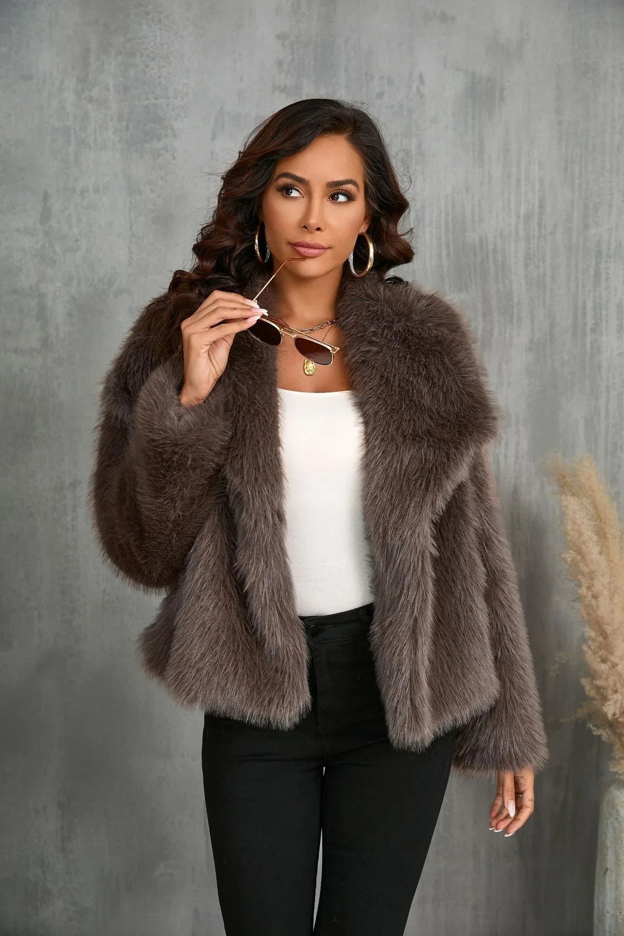 Woman holding sunglasses while wearing a brown faux fur cropped jacket