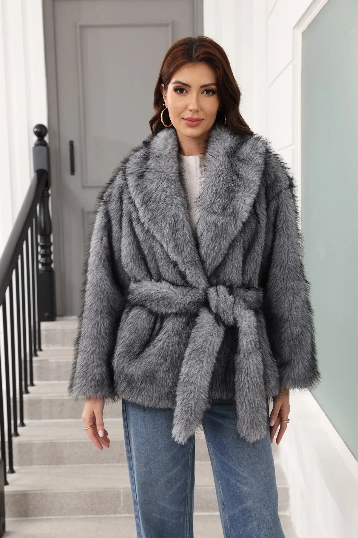 Woman wearing a grey faux fur jacket with a belted waist and notched lapel collar. Main image
