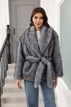 Woman wearing a grey faux fur jacket with a belted waist and notched lapel collar.