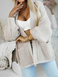 Woman posing in a beige knit cardigan with detailed sleeves and pockets.