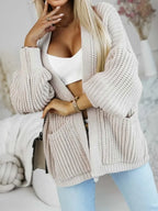 Woman posing in a beige knit cardigan with detailed sleeves and pockets.