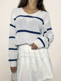 Woman's torso showing a white knit sweater with navy blue stripes and a v-neck.