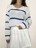Woman's torso showing a white knit sweater with navy blue stripes and a v-neck.