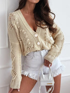 Woman wearing a beige cropped knit cardigan with V-neck and button closure.