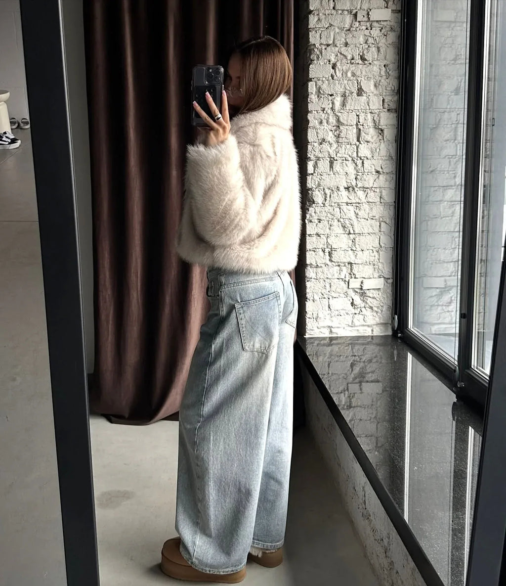 Side view of a woman showcasing the cropped silhouette of a cream faux fur jacket.