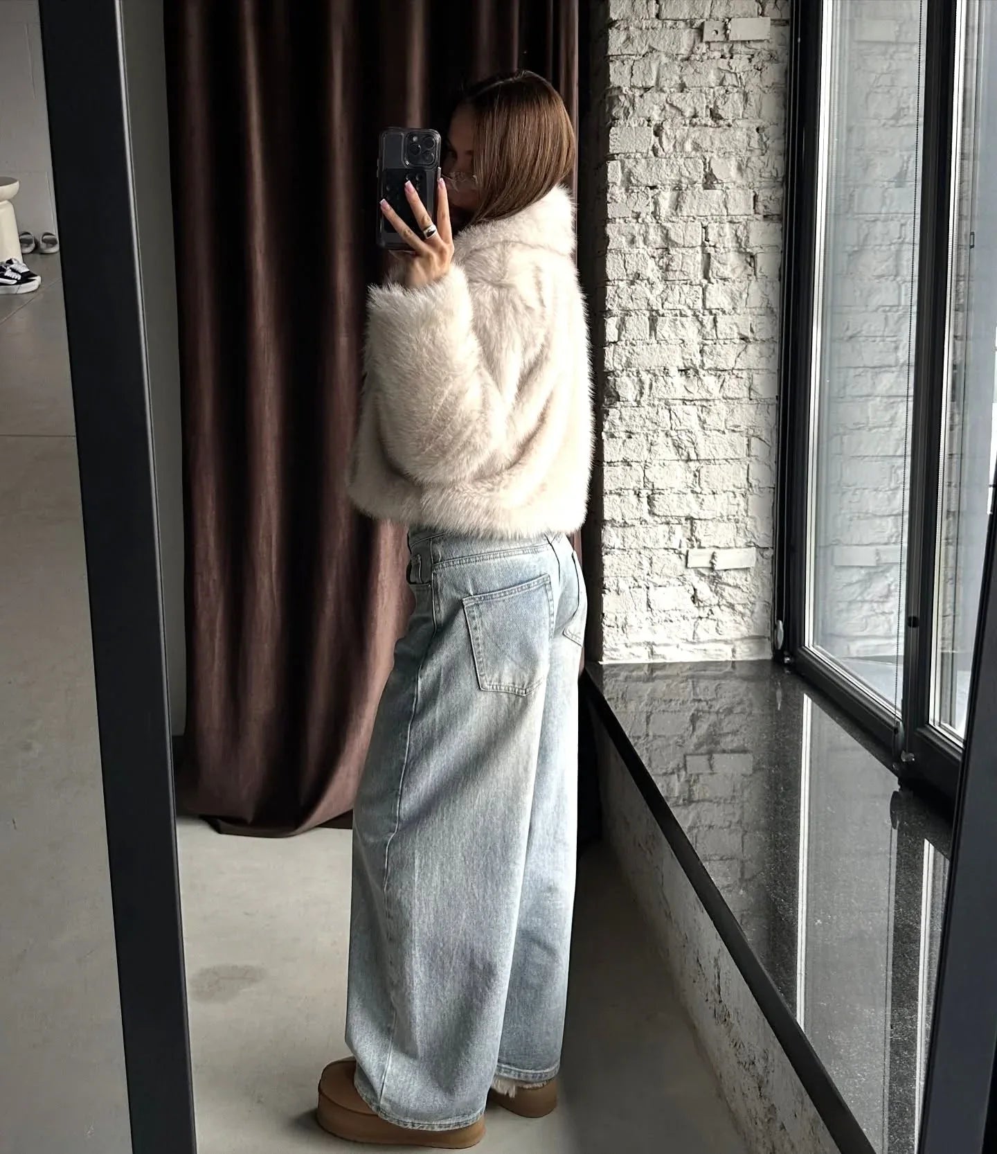 Side view of a woman showcasing the cropped silhouette of a cream faux fur jacket.