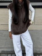 Close-up of a woman wearing a brown faux fur vest, white long-sleeved shirt, and white wide-leg jeans.