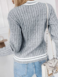 Back view of a woman wearing a grey v-neck cable knit sweater with white trim and an 'A' appliqué.