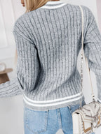 Back view of a woman wearing a grey v-neck cable knit sweater with white trim and an 'A' appliqué.