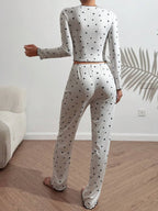 Woman sitting on a bed wearing a pink heart print pajama set.