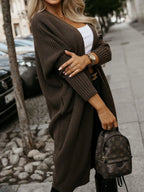 Woman posing with arms crossed, wearing a long brown ribbed knit cardigan and black pants.