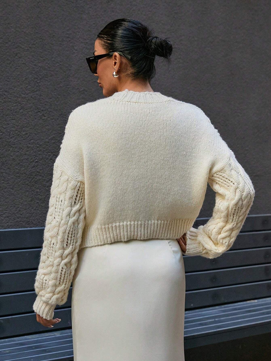Woman wearing a cream cable knit cropped cardigan with pearl buttons and a matching cream slip skirt.