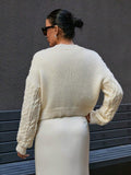 Back view of a woman in a cream cable knit cropped cardigan with textured sleeves.