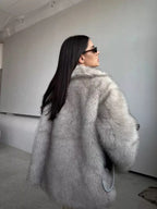 Rear view of a woman in a grey faux fur coat, showcasing its voluminous sleeves and soft texture.