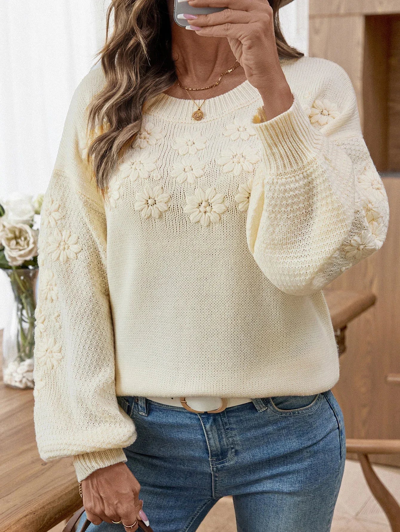 Close-up of a cream knit sweater with intricate 3D floral embroidery.