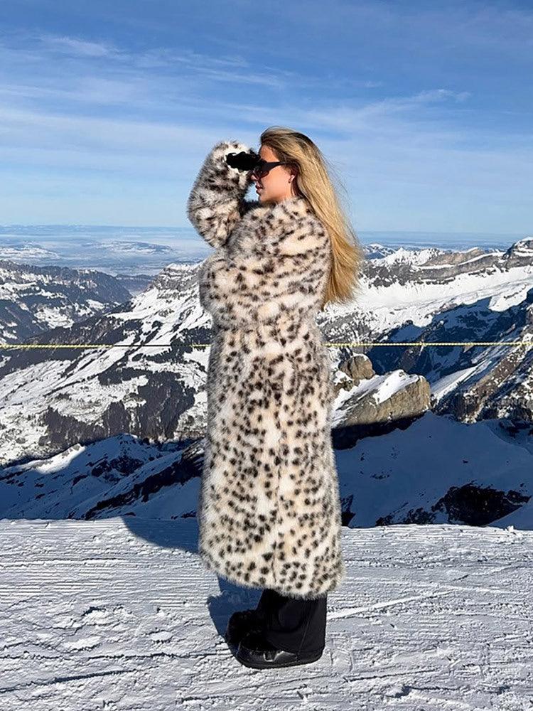 Woman wearing a long leopard print faux fur coat looking through binoculars on a snowy mountain.