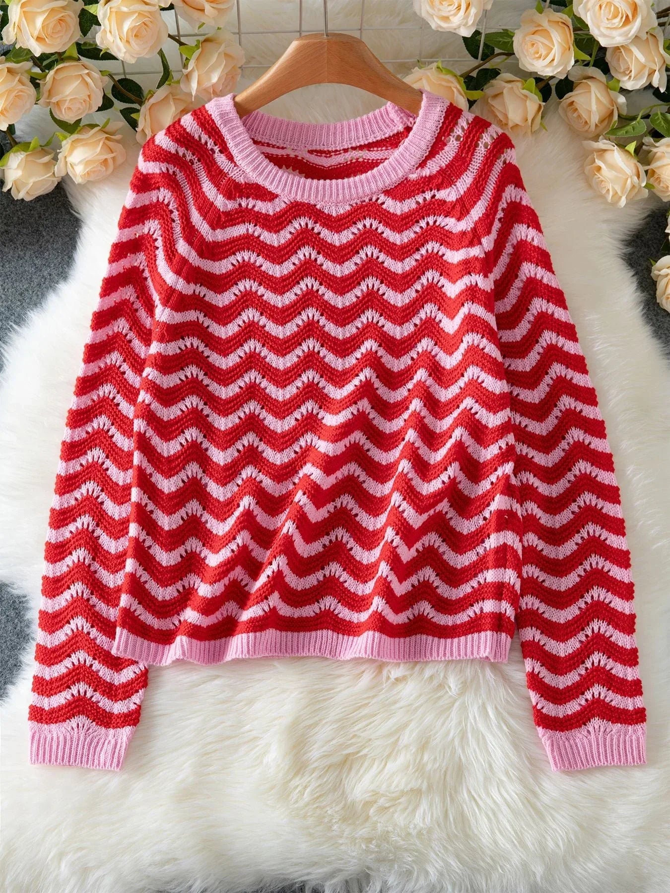 Red and pink chevron knit sweater laid flat on a white fluffy rug with flowers